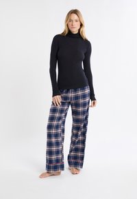 Dolcevita nero a maniche lunghe realizzato in tessuto morbido, abbinato a pantaloni da lounge blu a quadri con strisce bianche, rosse e beige, con una vestibilità comoda.