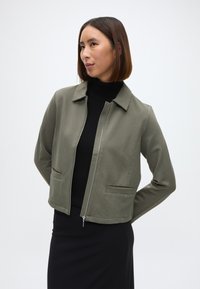 Ζακέτα μπορντό από υφασμάτινο ύφασμα με φερμουάρ, χαρακτηριστικά με μυτερό γιακά, δύο μπροστινές τσέπες και κοντό σχέδιο.