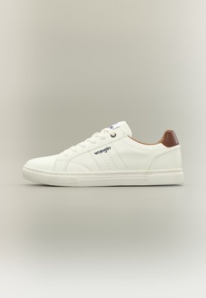 Baskets blanches basses avec lacets, languette de talon marron, logo Wrangler sur le côté et semelle en caoutchouc texturée sur fond neutre.