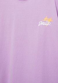 Tissu violet clair avec un petit texte stylisé blanc et deux formes jaunes en forme d'étoile dans la partie supérieure droite.