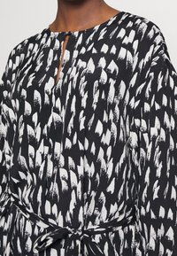 Schwarzes Kleid mit einem auffälligen weißen Pinselstrichmuster, Rundhalsausschnitt mit einem Schlüssellochdetail und einer gebundenen Taille für eine verstellbare Passform.