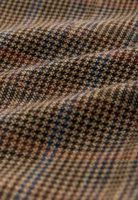 Tissu en laine avec un motif pied-de-poule marron, beige, bleu et rouge, montrant la texture et les plis en gros plan.
