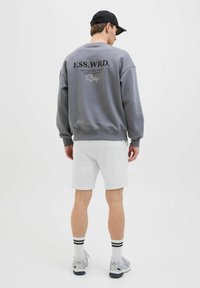 Sudadera gris con estampado negro en la parte trasera, combinada con pantalones cortos gris claro. La sudadera cuenta con puños y dobladillo acanalados.