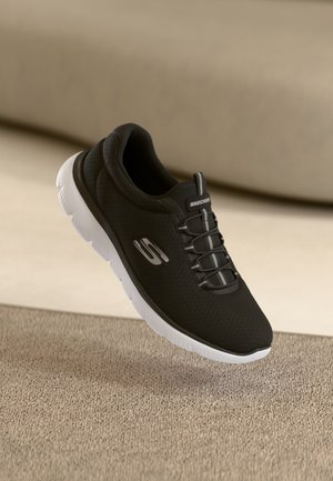 Schwarzer Skechers-Sneaker mit weißer Sohle, elastischen Schnürsenkeln und Logo an der Seite, platziert auf einer hellbraunen, strukturierten Oberfläche.