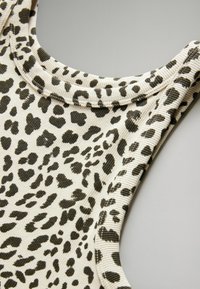 Kremvärd leopardmönstrad ärmlös topp med svarta prickar. Har ribbat mönster och rundad halsringning. Detaljerad sömnad längs kanterna.