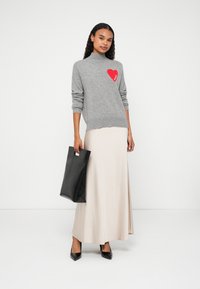 Szürke kötött pulóver piros szív mintával, bézs maxiszoknya, fekete bőr táska és fekete magassarkú cipő.