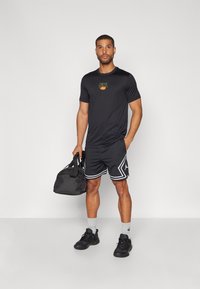 Svart t-skjorte med korte ermer fra Nike med logo, svarte shorts med hvite detaljer, svarte joggesko og en svart treningsbag. Minimalistisk design.