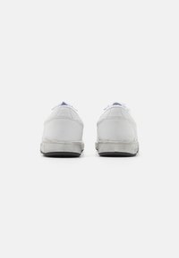 White leather sneakers with a low profile, featuring a smooth texture, rubber soles, and light blue accents on the tongue and lacing.
