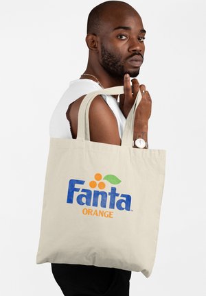 Beżowa torba tote z płótna z logo "Fanta" w niebieskim i pomarańczowym kolorze, zdobiona zielonym wzorem liścia. Torba ma długie uchwyty do łatwego noszenia.
