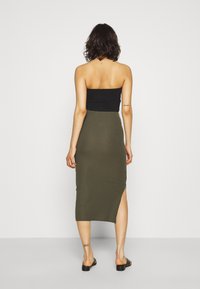 Černý top bez ramínek, spárovaný s olivově zelenou midi sukni s žebrováním a bočním rozparkem. Doplněno viditelným tetováním na kotníku.