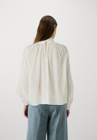 Hvit bluse med vertikale striper og nøkkelhullbak. Har vide ermer og en avslappet passform, laget av et lett stoff.