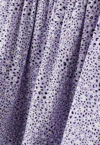 Tissu lavande parsemé de petites taches noires irrégulières, rassemblé en plis doux créant un motif texturé.