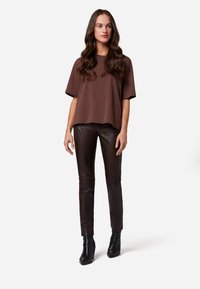 Bruine katoenen t-shirt met korte mouwen, gecombineerd met nauwsluitende donkerbruine leren broek en zwartehakken enkellaarsjes. Eenvoudig, modern ontwerp.
