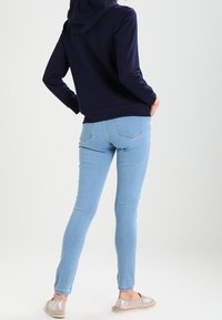 Sudadera navy, diseño ajustado, bolsillo canguro, combinada con jeans ajustados de color azul claro y alpargatas plateadas, vista desde la parte posterior.