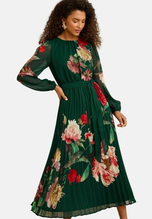 Langes plissiertes Kleid aus dunkelgrüner Chiffon, verziert mit großen floralen Mustern in Pink, Rot und Gelb, mit langen Ärmeln und einer taillierten Passform.
