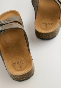Sandales en cuir marron avec des brides tissées, une semelle en liège et un intérieur doux. Taille notée comme 42 avec le nom de la marque visible.