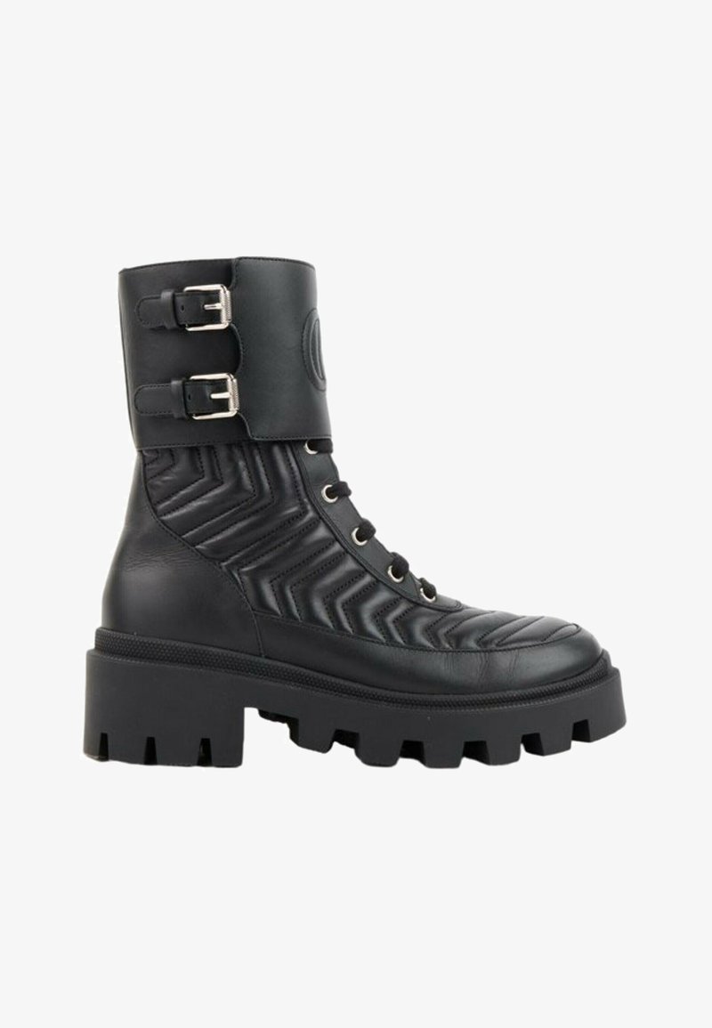 Botte de combat en cuir noir avec semelle épaisse à crampons, motif matelassé en chevron, lacet à l’avant et deux boucles argentées réglables en haut.