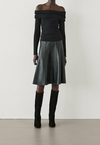 Top nero off-the-shoulder con maniche lunghe aderenti abbinato a una gonna di pelle nera plissettata e stivali al ginocchio in suede nero.