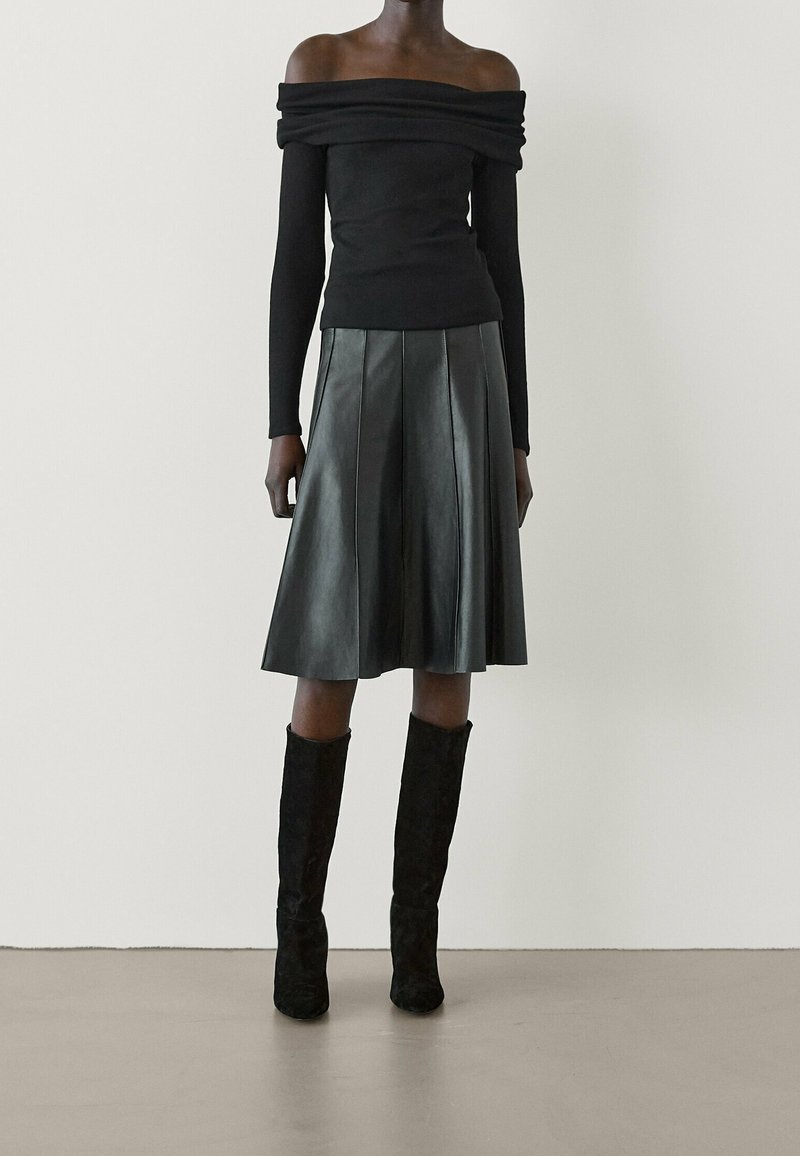 Top nero off-the-shoulder con maniche lunghe aderenti abbinato a una gonna di pelle nera plissettata e stivali al ginocchio in suede nero.