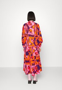 Lang jurk met een gelaagd ontwerp in felle roze, oranje en paarse bloemmotieven. Lange mouwen en een gathered taille-detail.