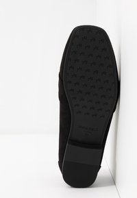 Semelle de chaussure en daim noir avec une semelle en caoutchouc texturée, arborant un logo embossé et la taille 37. Léger arrondi à l\'avant-pied et design de talon plat.