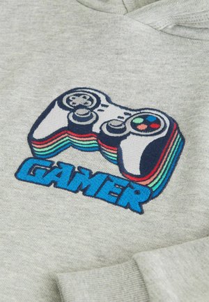 Hoodie gris arborant un contrôleur de jeu vidéo brodé au-dessus du mot "GAMER" en bleu gras, avec des bandes colorées sur le contrôleur.