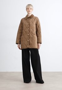Braun gesteppte Jacke mit Kragen, Knopfverschluss und seitlichen Taschen. Kombiniert mit schwarzen weit geschnittenen Hosen. Glatte Textur, lässiges Design.