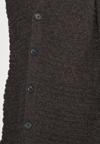 Cardigan lavorato a maglia marrone scuro con un motivo texture, sei bottoni neri sul davanti e una finitura morbida a coste.