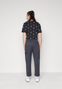 Black graphic T-shirt with scattered prints, paired with gray cargo pants featuring side pockets. White sneakers complete the outfit.