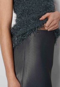 Flauschiger, dunkelgrauer, kurzer Pullover mit lockeren Fasern, kombiniert mit einem enganliegenden, dunkelgrauen Lederrock, der den Texturkontrast am Saum hervorhebt.