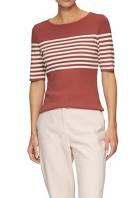 Top de punto rojo con mangas cortas, con rayas horizontales blancas en el pecho. Textura suave y escote redondo. Combinado con pantalones claros.