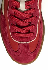 Red athletic shoe with a suede and synthetic upper, lace closure, and rubber outsole. Features contrasting stitching and a textured surface.