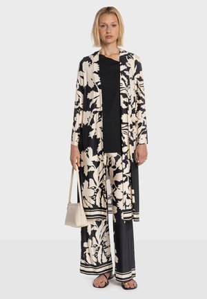 Abito con fantasia floreale nera e crema, pantaloni a gamba larga e cardigan lungo aperto. Tessuto strutturato con accenti neri e top nero tinta unita.