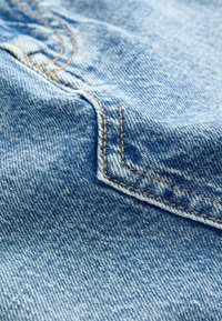Denim tkanina u svijetloplavoj boji, s vidljivim šavovima u kontrastnoj žutoj nijansi i teksturiranim uzorcima površine.