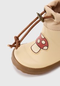 Gummistøvel i beige med brun teksturert såle. Har et rødt soppgrafikk på siden. Lær snøringsdetalj på toppen.
