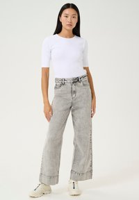 White fitted top paired with high-waisted, faded gray wide-leg jeans, featuring a clean hem and subtle distressing. Sneakers with accents.