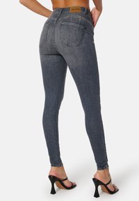 Smala mörkgrå denimjeans med bakfickor och en medelhög midja, ihopparat med svarta klacksandaler för kontrast.