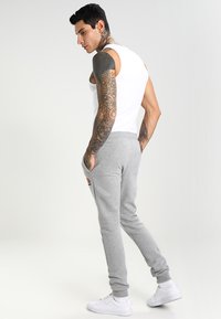 Pantalones de chándal grises con un diseño ajustado, fabricados en tela suave. Con bolsillos laterales y puños elásticos, presentan un pequeño logo en el muslo izquierdo.