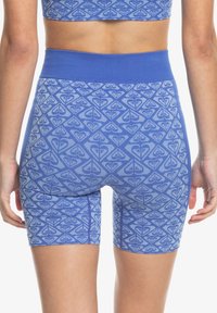 Pantalones cortos activos de color azul con un diseño geométrico en tonos azules más claros. Tienen una cintura alta y están confeccionados con un material elástico y texturizado.