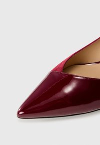 Burgundy patent leather kengännokka, jossa on pehmeä mokkanahka-aksentti kantapäässä, ja se on varustettu sileällä pinnalla ja hoikalla siluetilla.