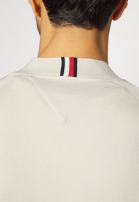 Sudadera gris con cuello acanalado que presenta rayas rojas, blancas y negras. Textura suave, ajuste clásico y detalle de costura en forma de V.