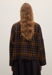 Plaid jacket in dark blue and mustard yellow, made from soft fabric, featuring a relaxed fit and drop shoulders, with a cropped length.