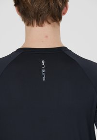 Zwarte sport t-shirt van textuurstof, met raglanmouwen en een reflecterende "ELITE LAB" logo op de bovenrug.