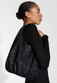 Zwarte, met pailletten bedekte stoffen tote bag met een zachte, pluchen vorm. Heeft een brede opening en een gestructureerde detail, gecombineerd met een geribde zwarte lange mouwen top.