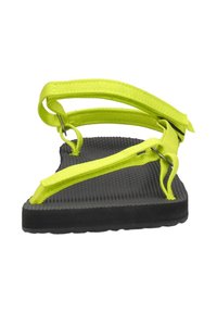 Chanclas de goma negras con suela texturizada; presentan correas de tela amarilla brillante y herrajes plateados, diseñadas para una fácil colocación.
