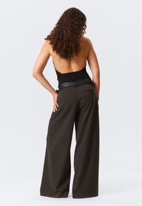 Pantaloni a gamba larga in verde oliva scuro, realizzati in tessuto morbido. Presentano una cintura nera e due tasche posteriori, evidenziando una vestibilità rilassata.