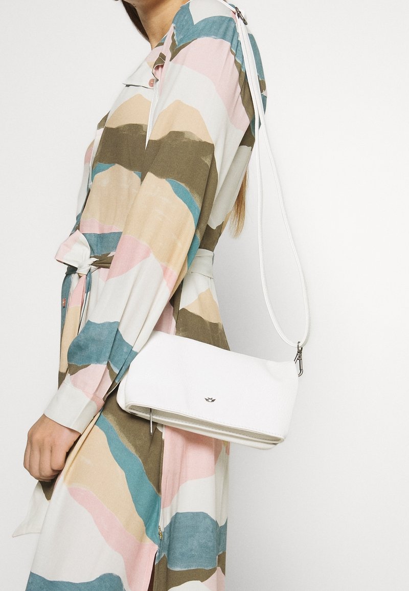 Borsa a mano bianca in pelle con una forma rettangolare slim e una tracolla staccabile, mostrata su un vestito a fantasia multicolore.