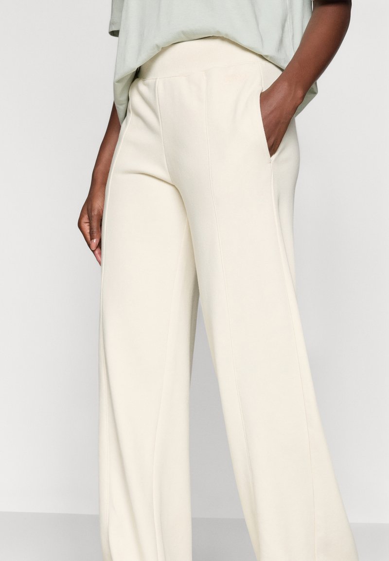 Pantaloni a gamba larga color crema realizzati in morbido tessuto, con una texture liscia e tasche laterali, dotati di una cintura elastica per il massimo comfort.