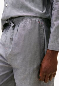 Graues gestreiftes Pyjamaset mit elastischem Bund, Kordelzug-Detail und kleinen Logoakzenten in Rot und Blau. Weicher, leichter Stoff.