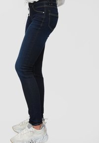 Pantalones vaqueros ajustados de color azul oscuro con una textura suave, que cuentan con una cintura de altura media, bolsillos frontales y un sutil detalle de costura a lo largo de las costuras.